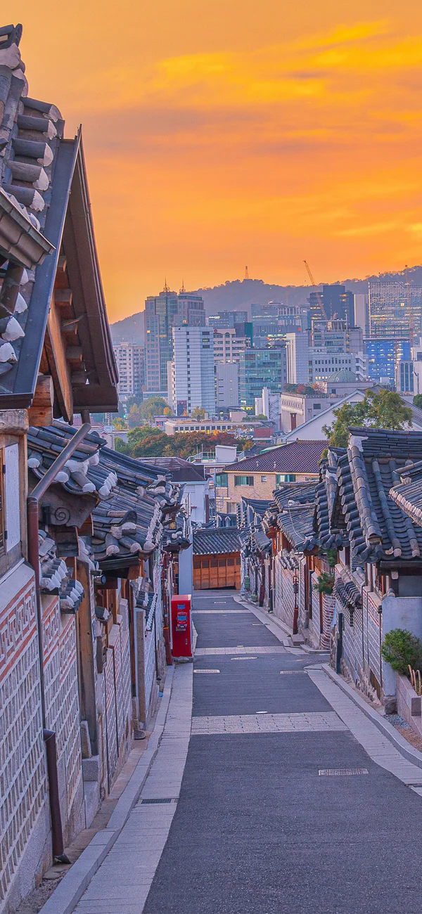 Auringonlasku Bukchon Hanok -kylän yllä Soulissa Etelä-Koreassa, kaupungin siluetti taustalla
