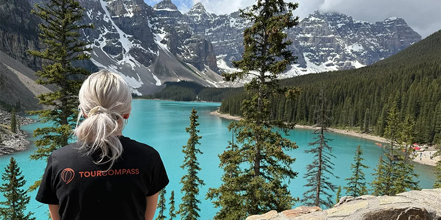 Nainen TourCompass-t-paidassa katselee vettä Lake Louisen rannalla Kanadassa