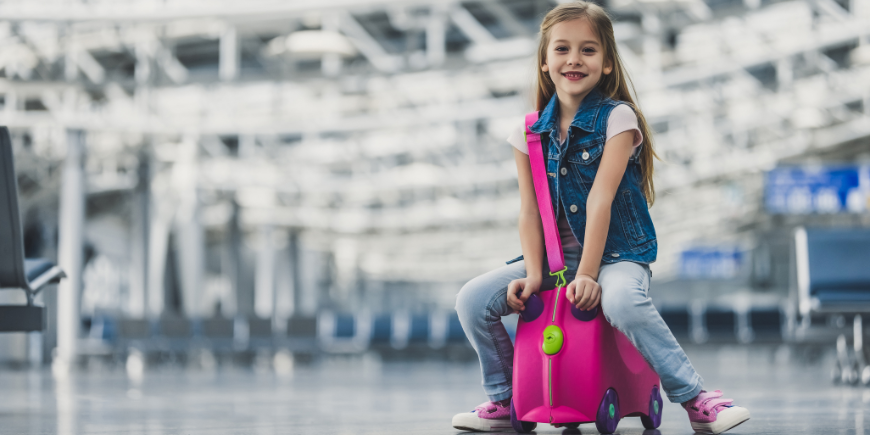 Lapsi istuu matkalaukun päällä lentokentällä