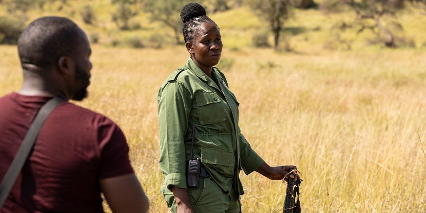Nainen seisoo kivääri kädessään savannilla