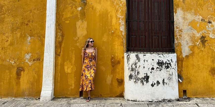 Oranssipukuinen nainen nojaa oranssiin seinään Izamalissa, Meksikossa.