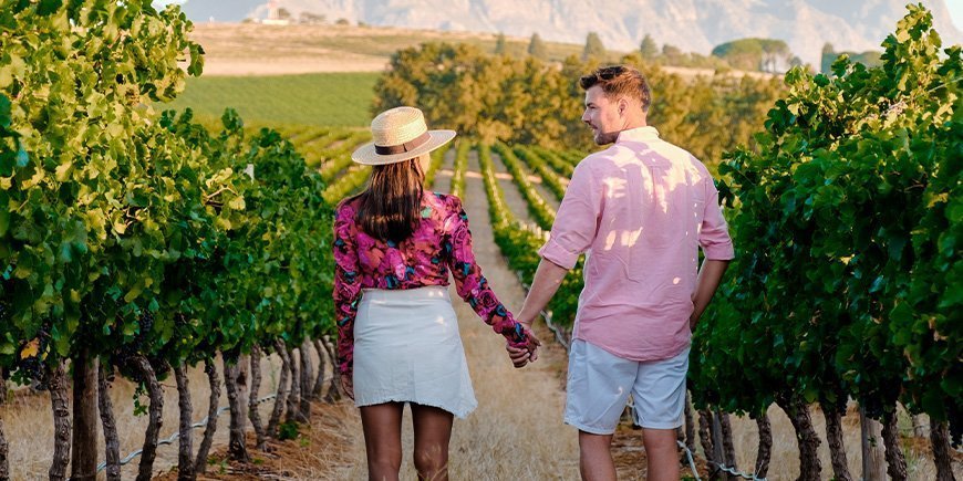 Nainen ja mies kädestä pitäen viinitarhassa Etelä-Afrikassa