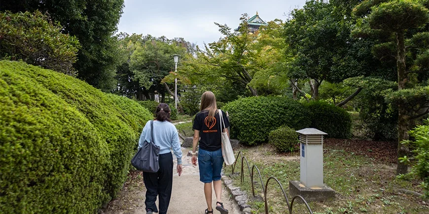 Japanilainen opas ja TourCompassin työntekijä kävelevät Osakan linnan lähellä Japanissa